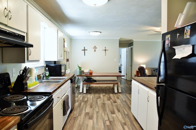 kitchen featuring black appliances, crown molding, under cabinet range hood, butcher block countertops, and white cabinetry