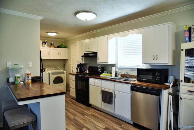 kitchen featuring wooden counters, under cabinet range hood, washer / dryer, black appliances, and a sink