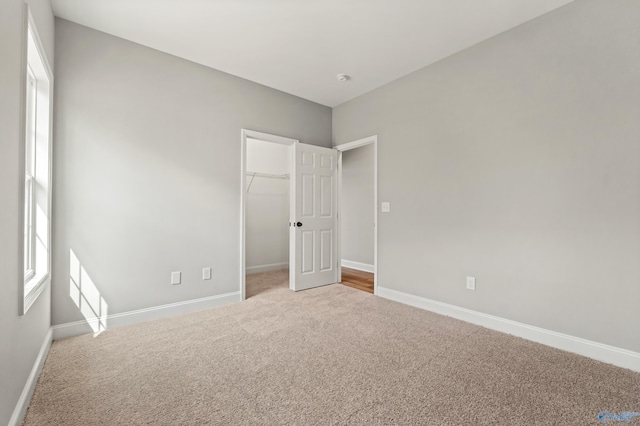 unfurnished bedroom featuring a spacious closet, multiple windows, carpet flooring, and baseboards