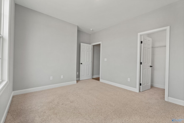 unfurnished bedroom featuring a spacious closet, carpet, and baseboards