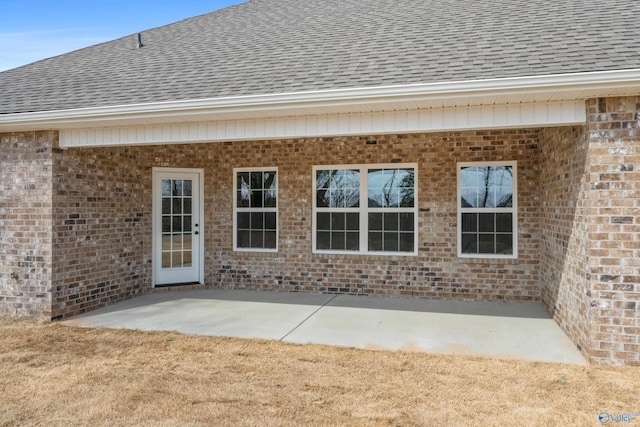 exterior space featuring a patio area, a shingled roof, and brick siding