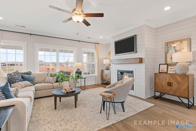 living room featuring a glass covered fireplace, wood finished floors, visible vents, and recessed lighting