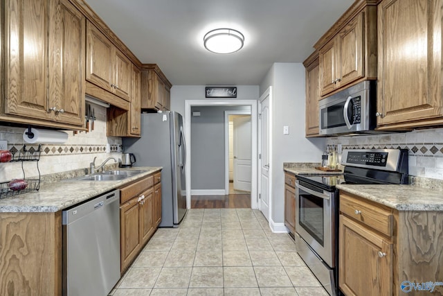 kitchen with light tile patterned flooring, sink, backsplash, light stone counters, and stainless steel appliances