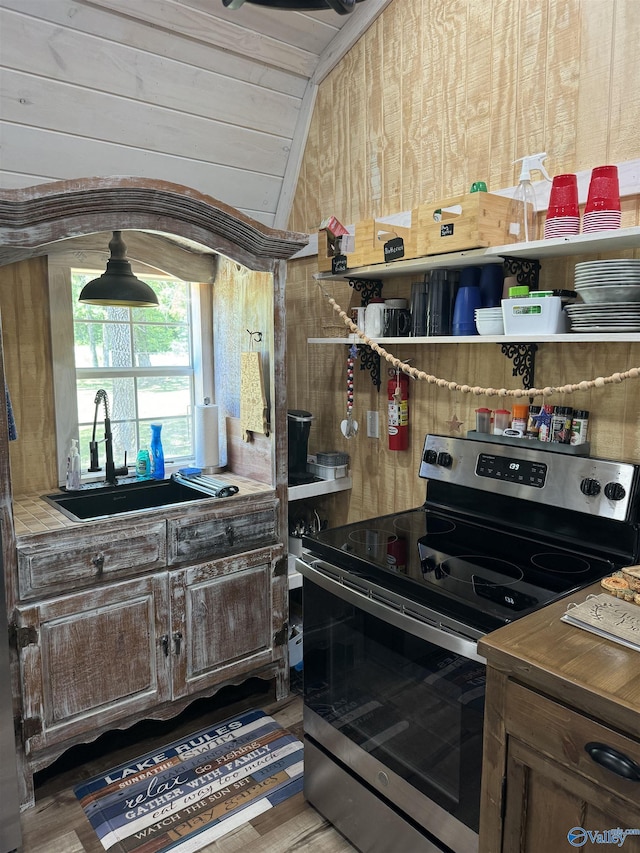 kitchen with vaulted ceiling, wood walls, sink, stainless steel range with electric cooktop, and wood ceiling