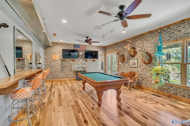 rec room with brick wall, light hardwood / wood-style flooring, and a healthy amount of sunlight