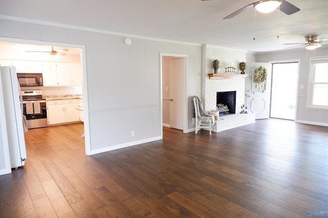 unfurnished living room with dark wood-style flooring, a brick fireplace, a ceiling fan, baseboards, and ornamental molding