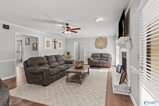 living room with a fireplace, crown molding, ceiling fan, and wood finished floors