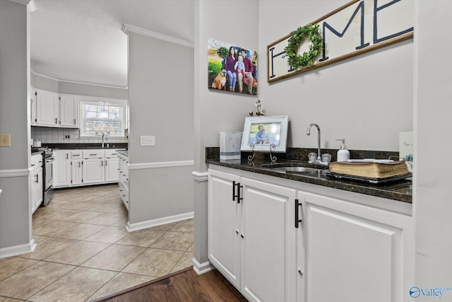 kitchen with decorative backsplash, stainless steel stove, white cabinets, and a sink