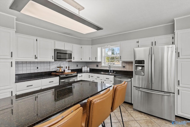 kitchen featuring a sink, backsplash, appliances with stainless steel finishes, light tile patterned floors, and white cabinets