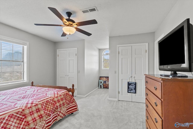 bedroom with a textured ceiling, visible vents, baseboards, a ceiling fan, and light carpet