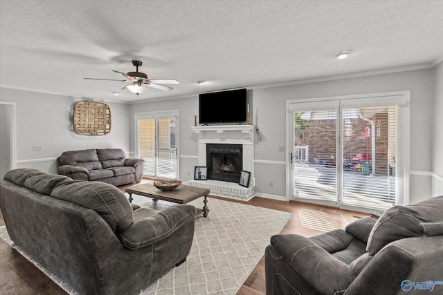 living area with a fireplace, ornamental molding, ceiling fan, and wood finished floors