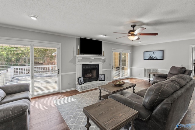living room with a ceiling fan, a fireplace, wood finished floors, a textured ceiling, and visible vents