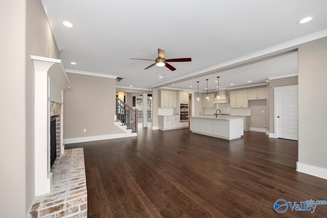 unfurnished living room with stairway, baseboards, a fireplace, dark wood-style flooring, and a sink