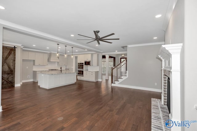 unfurnished living room featuring a fireplace, crown molding, dark wood-type flooring, ceiling fan, and a barn door