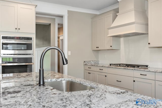 kitchen with a sink, tasteful backsplash, stainless steel appliances, light stone countertops, and custom exhaust hood