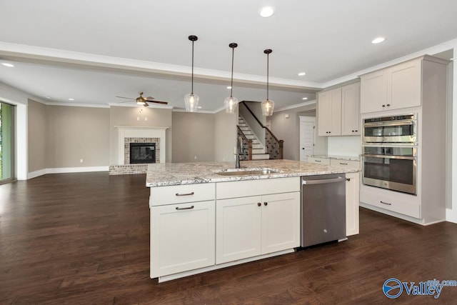 kitchen with a fireplace, dark wood-style flooring, a sink, appliances with stainless steel finishes, and crown molding