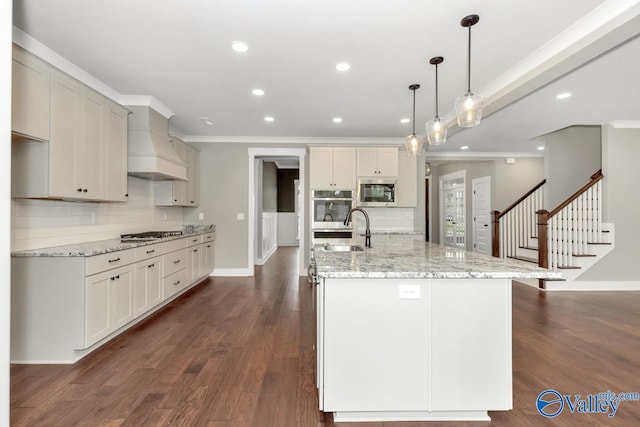 kitchen with appliances with stainless steel finishes, a large island with sink, dark wood-type flooring, custom range hood, and backsplash