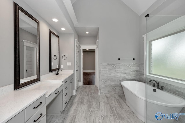 full bathroom with vanity, tile walls, a freestanding bath, a spacious closet, and vaulted ceiling