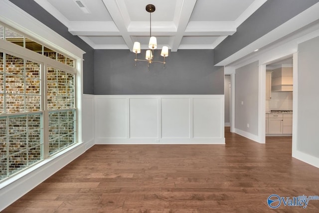 unfurnished dining area with a chandelier, beamed ceiling, coffered ceiling, and wood finished floors