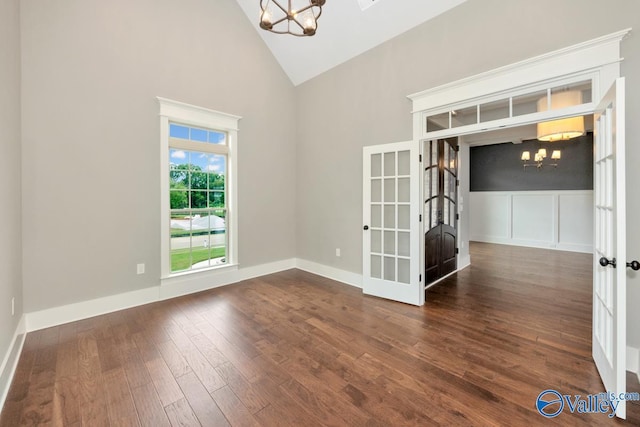 spare room with baseboards, a notable chandelier, dark wood finished floors, and high vaulted ceiling