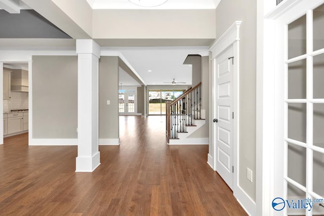 foyer featuring stairway, a ceiling fan, wood finished floors, baseboards, and decorative columns