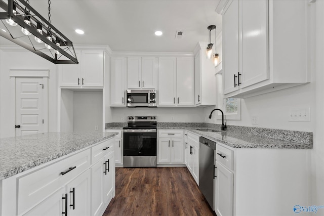 kitchen with white cabinets, appliances with stainless steel finishes, decorative light fixtures, sink, and light stone counters