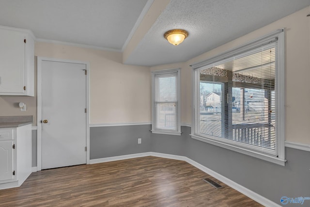 unfurnished dining area with ornamental molding, dark wood-type flooring, and a textured ceiling