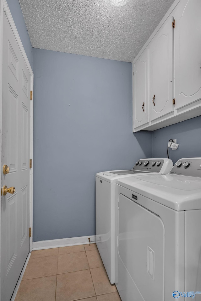 laundry room featuring light tile patterned flooring, cabinets, washer and clothes dryer, and a textured ceiling