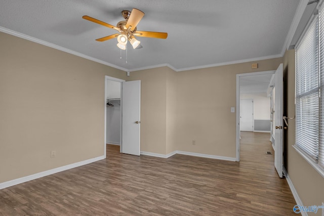 unfurnished bedroom featuring wood-type flooring, a spacious closet, a textured ceiling, ornamental molding, and ceiling fan