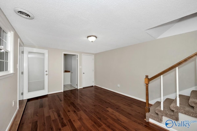 interior space featuring a textured ceiling, visible vents, baseboards, wood finished floors, and stairway