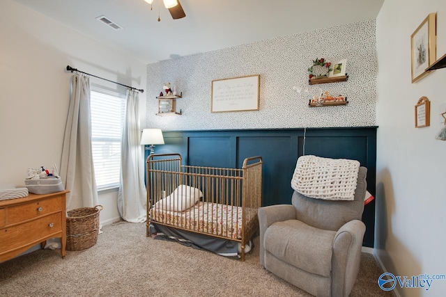 carpeted bedroom with ceiling fan and a nursery area
