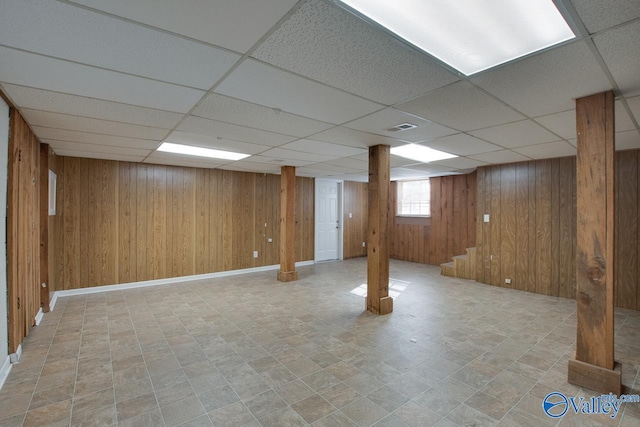 basement featuring a drop ceiling and wooden walls