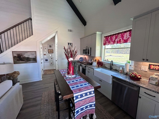 kitchen featuring appliances with stainless steel finishes, white cabinetry, sink, light stone countertops, and beam ceiling