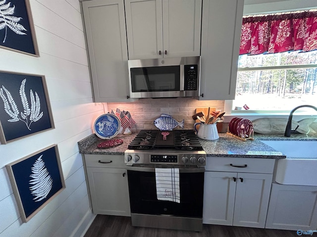 kitchen featuring appliances with stainless steel finishes, sink, white cabinets, light stone countertops, and dark wood-type flooring