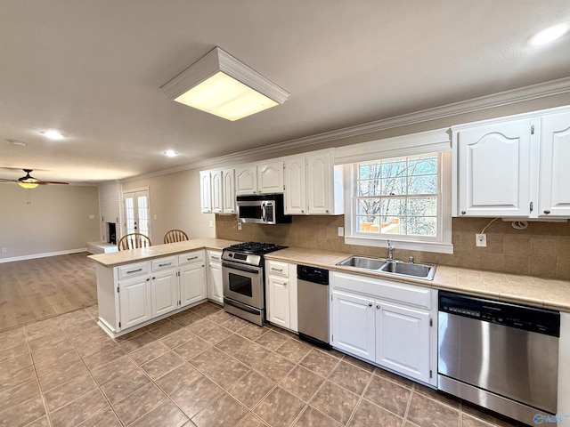 kitchen featuring a peninsula, a sink, light countertops, appliances with stainless steel finishes, and tasteful backsplash