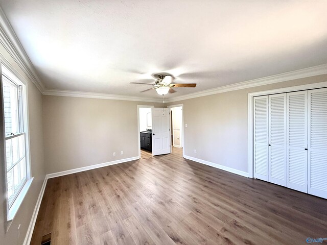 unfurnished bedroom with wood finished floors, visible vents, baseboards, ornamental molding, and a closet