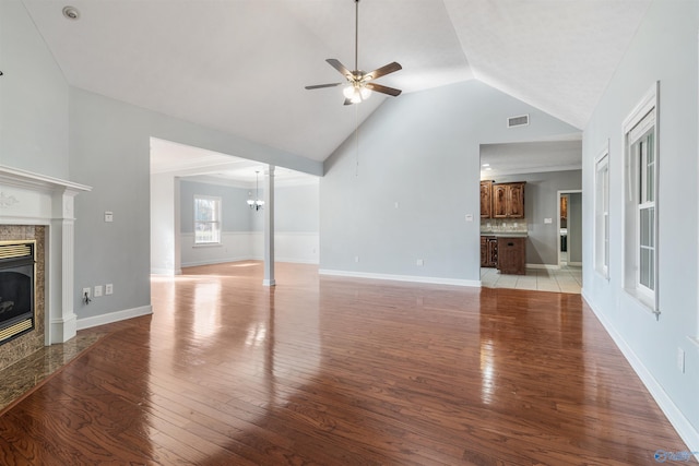 unfurnished living room featuring a fireplace, high vaulted ceiling, light hardwood / wood-style floors, and ceiling fan with notable chandelier