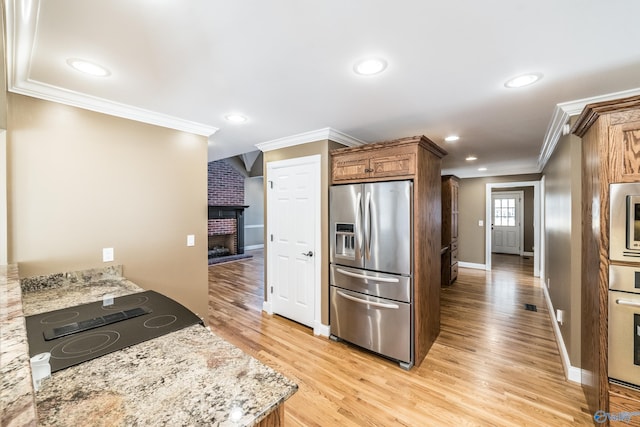 kitchen with stainless steel appliances, light stone counters, light hardwood / wood-style flooring, a fireplace, and ornamental molding