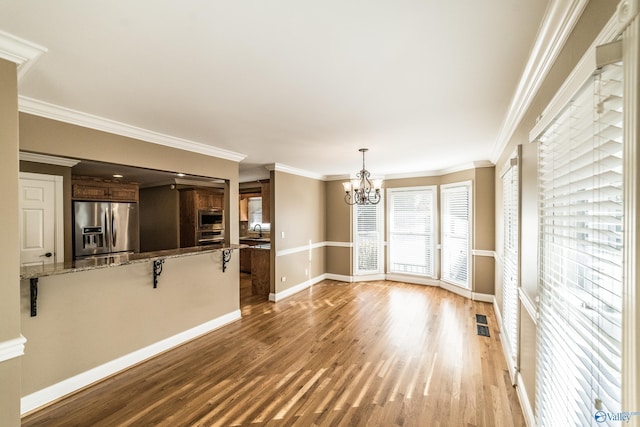 unfurnished living room featuring hardwood / wood-style floors, a notable chandelier, sink, and crown molding