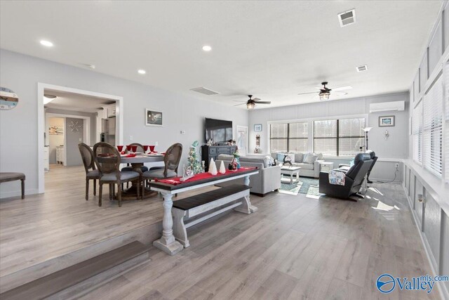 living room with light hardwood / wood-style floors, a wall unit AC, and ceiling fan