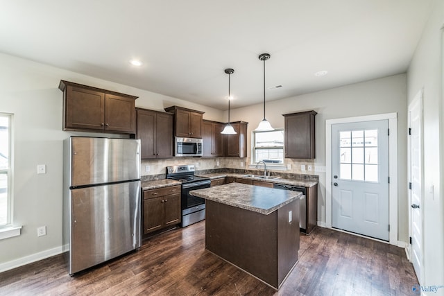 kitchen featuring pendant lighting, sink, dark wood-type flooring, stainless steel appliances, and a kitchen island