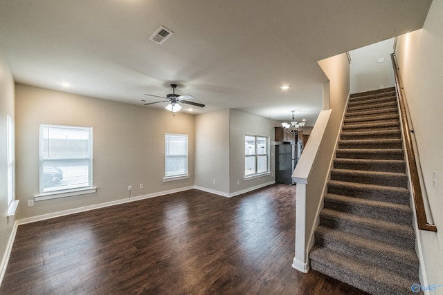 unfurnished living room with ceiling fan with notable chandelier and dark hardwood / wood-style flooring