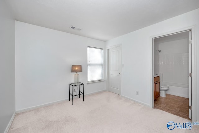 unfurnished bedroom featuring light colored carpet and ensuite bath