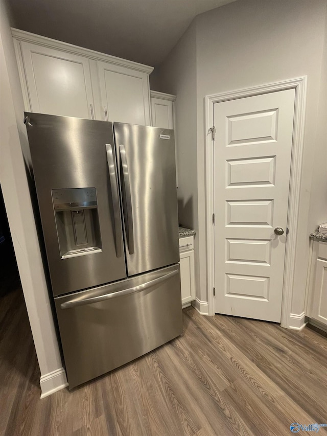 kitchen with stainless steel refrigerator with ice dispenser, light stone counters, white cabinets, and dark hardwood / wood-style flooring