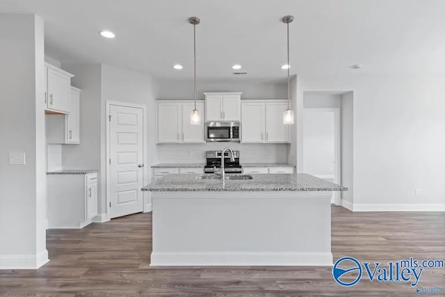 kitchen with a kitchen island with sink, sink, light stone countertops, and white cabinets