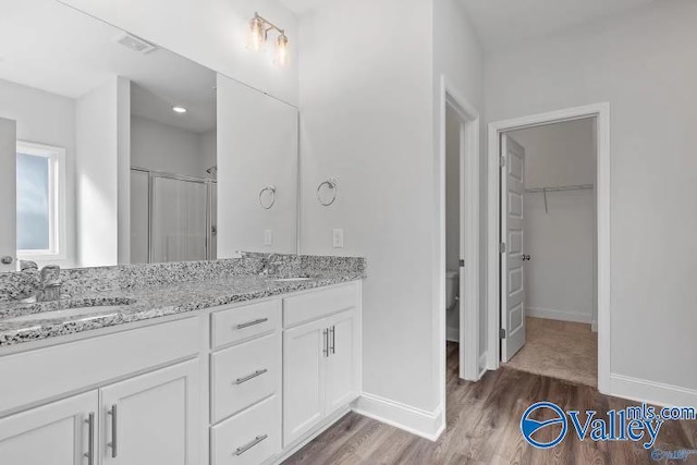 bathroom featuring wood-type flooring, toilet, a shower with shower door, and vanity