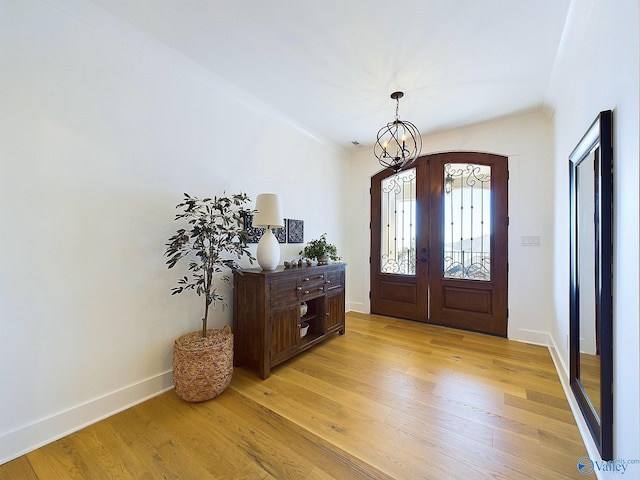 foyer entrance with crown molding, french doors, an inviting chandelier, and light wood-type flooring