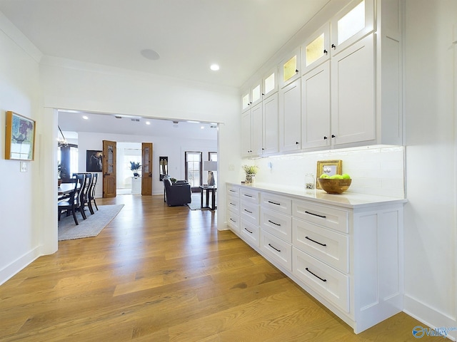 kitchen featuring tasteful backsplash, white cabinetry, light hardwood / wood-style flooring, and ornamental molding