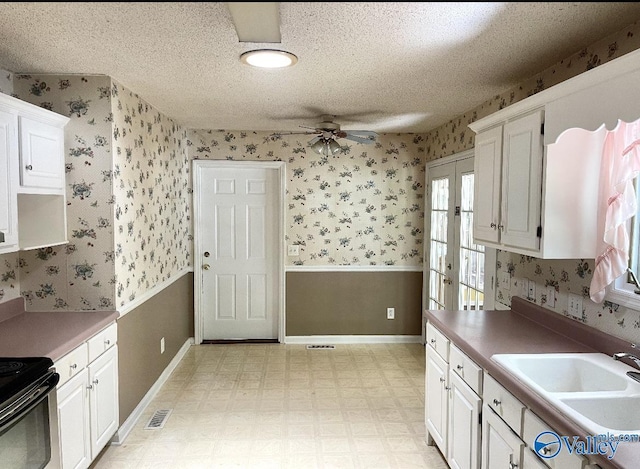 kitchen featuring white cabinetry, a sink, visible vents, and wallpapered walls