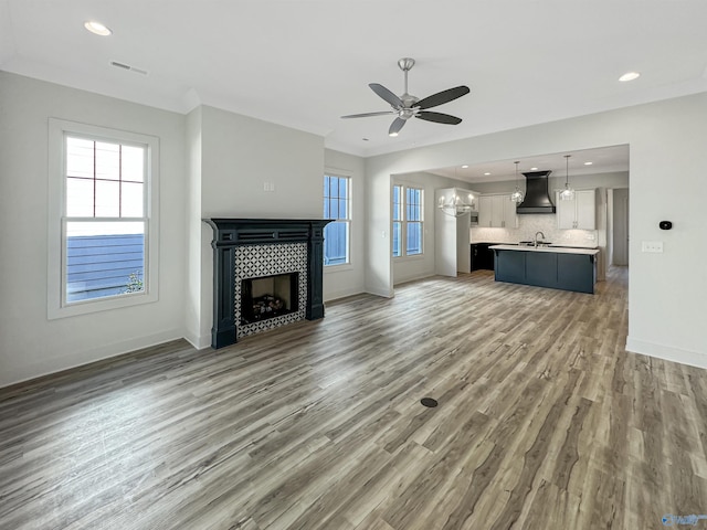 unfurnished living room featuring hardwood / wood-style floors, crown molding, ceiling fan with notable chandelier, and a tile fireplace